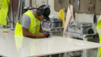 Shop worker with hearing and eye protection doing finishing work.